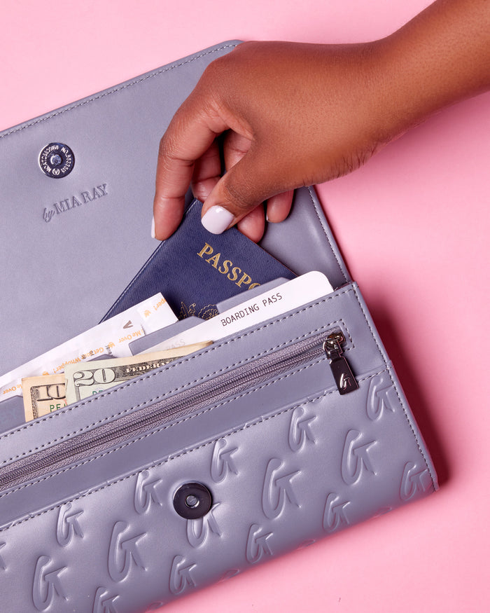 Gray Monogram Travel Wallet with embossed G pattern, holding a passport, boarding pass, cash, and cards on pink background.