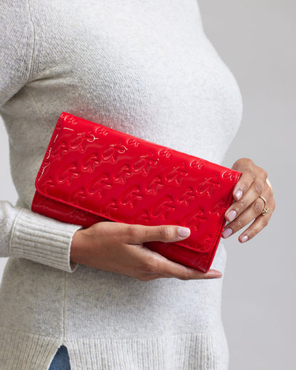 Red Monogram Travel Wallet with embossed logo pattern, held by a person in a light sweater.