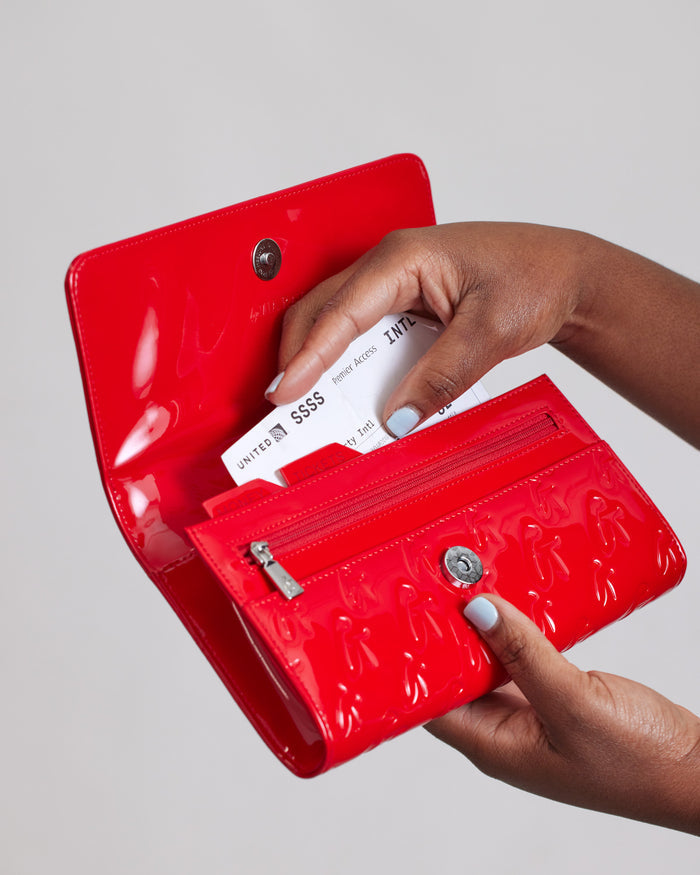 Red Monogram Travel Wallet with a glossy finish, featuring multiple card slots, a zippered compartment, and a snap button closure.