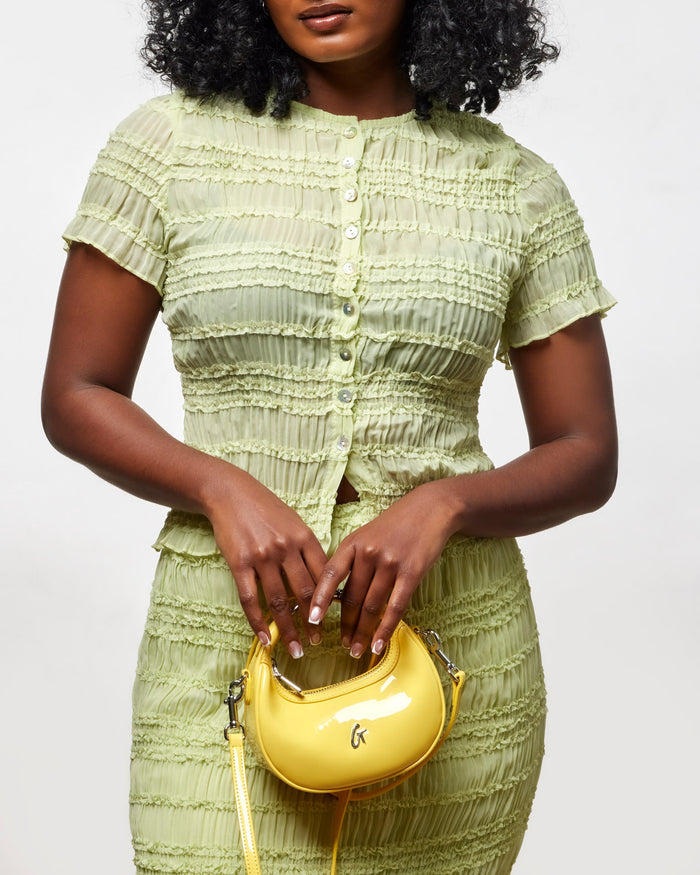 Chic woman in a textured green outfit holding a yellow Nano Mirror Hobo Bag, showcasing affordable luxury style.
