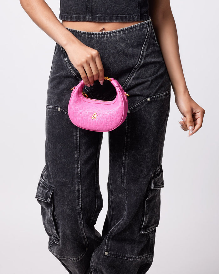 A person holding a small, hot pink Nano Pebble Hobo Bag with a gold "G" logo, against a plain background.