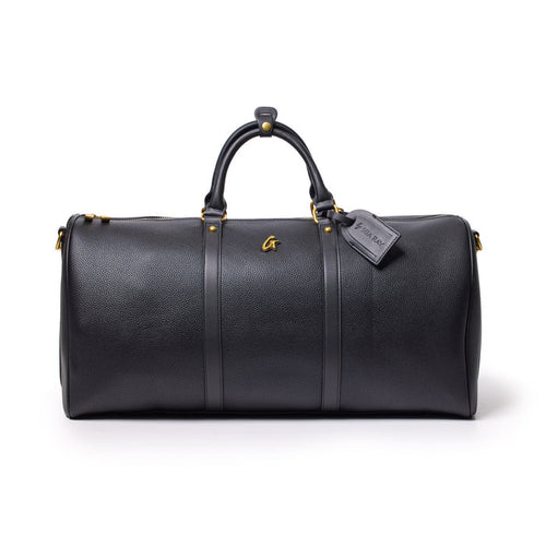 Black Pebble Duffle Bag with leather handles, gold accents, and a luggage tag, designed for travel and storage.