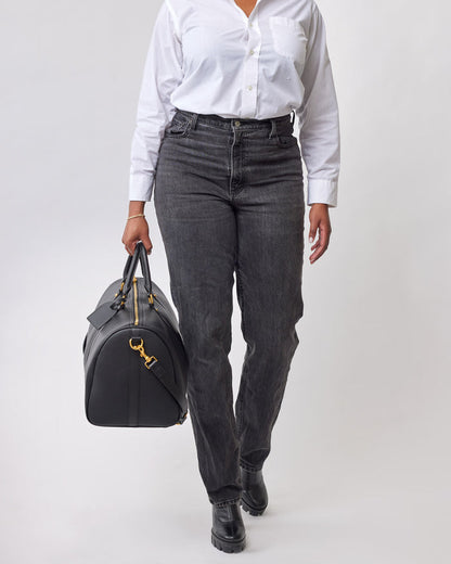 Black Pebble Duffle Bag with gold hardware, held by a person wearing a white shirt and black jeans.