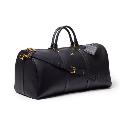 Black Pebble Duffle Bag with gold hardware, dual handles, adjustable shoulder strap, and luggage tag.