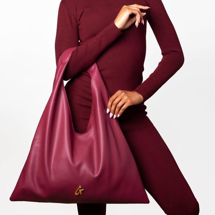 Burgundy pebble hobo shoulder bag held by a model, showcasing its stylish design and luxurious texture.