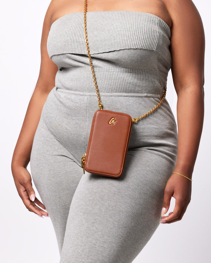 Brown pebble phone crossbody bag with gold chain strap and small gold logo, worn across a person's torso.