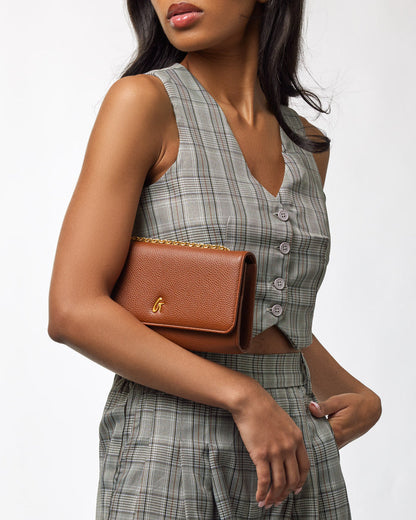 Brown Pebble Travel Wallet on a woman’s arm, featuring a gold chain and logo, with a plaid outfit.