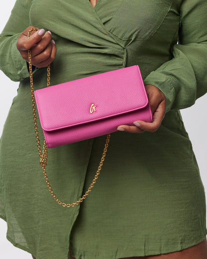 Pink Pebble Travel Wallet on a gold chain, held by a person in a green outfit, showcasing a vibrant, textured design.