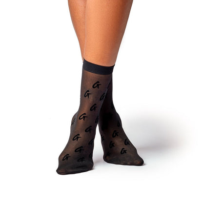 Black sheer logo socks with a repeating "G" pattern, worn by a person with crossed legs against a white background.