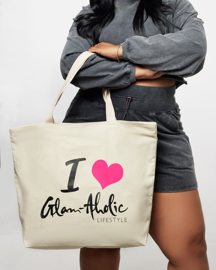 A woman holds a hot pink signature logo canvas tote bag with "I ♥ Glam-aholic Lifestyle" printed on it.