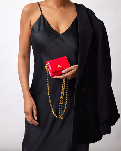 Red compact mirror with gold chain and logo, held by a woman in a black satin dress and blazer.