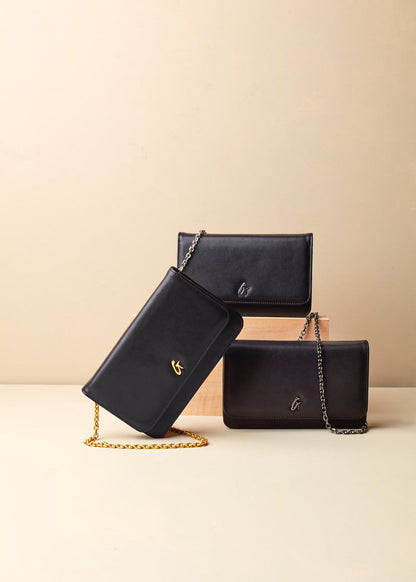 Black leather wallets with chain straps, featuring gold and silver logo accents, arranged on a beige surface.