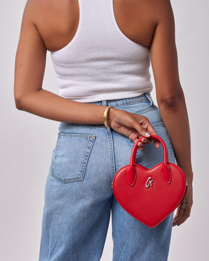 Red heart-shaped handbag held behind a woman's back, showcasing its stylish design and luxury appeal.