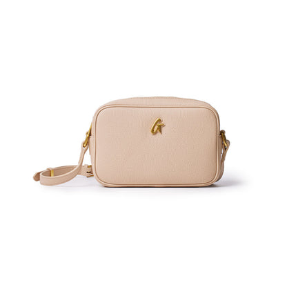Nude-colored Pebble Camera Bag with gold logo, adjustable strap, and textured leather finish.