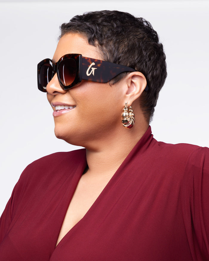 Stylish woman wearing tortoise shell sunglasses and statement earrings, showcasing a chic and confident look.
