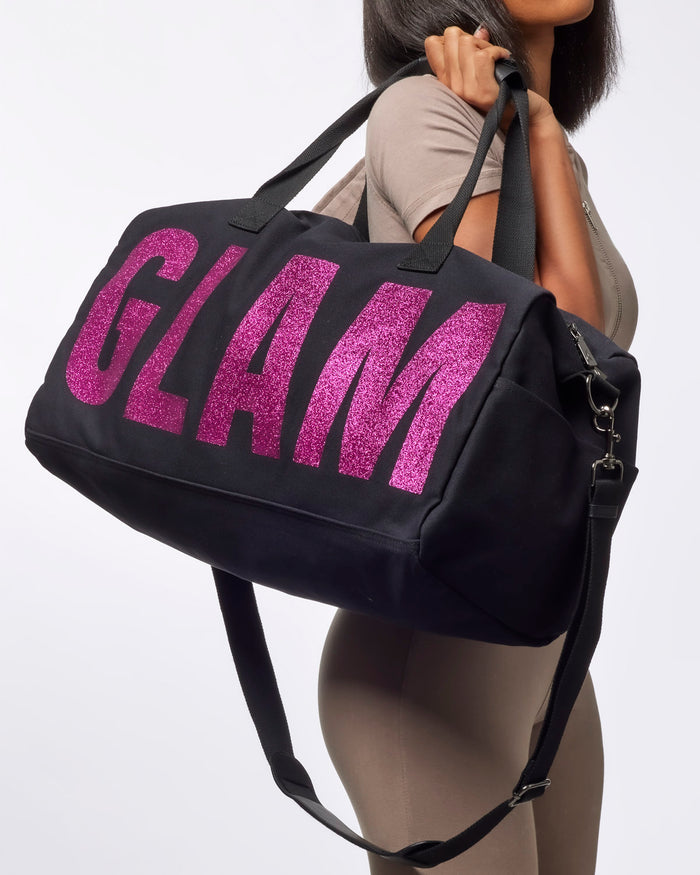 Black canvas duffle bag with bold pink glitter "GLAM" lettering, perfect for stylish travel or gym use.