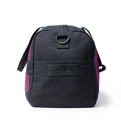 Black canvas duffle bag with pink accents and a front logo patch, featuring a zip closure and adjustable strap.