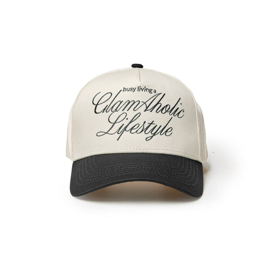 Black trucker hat with cream front featuring the text "busy living a GlamAholic Lifestyle" in stylish script.