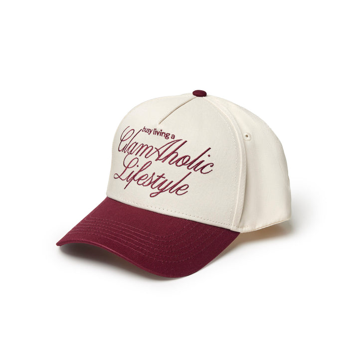 Burgundy trucker hat featuring "Busy Living a Glam-Aholic Lifestyle" embroidered in stylish script.